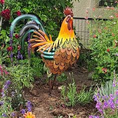 a colorful rooster statue standing in the middle of flowers