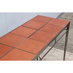 an orange tiled table sitting on the side of a building next to a sidewalk with no one around it