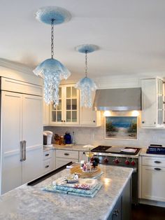 a kitchen with white cabinets and marble counter tops, an island in front of the refrigerator