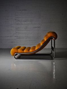 an orange chaise lounge chair sitting in front of a brick wall and concrete floor