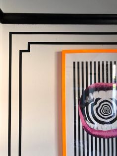 an art piece is hanging on the wall next to a framed painting with black and white stripes