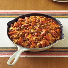 a skillet filled with chili and cheese on top of a striped place mat next to a bowl