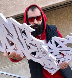 a man in red hoodie and sunglasses holding up letters