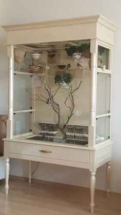 a white cabinet with glass doors and plants in it on top of a hard wood floor