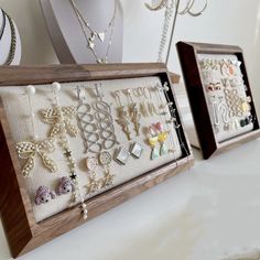 two wooden frames filled with jewelry on top of a white table next to other items