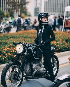 a woman in a suit and helmet sitting on a motorbike next to some flowers