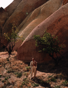 a man standing next to a tree in the middle of a rocky area with trees growing out of it