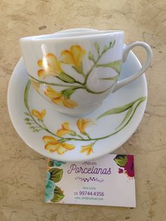 a cup and saucer with yellow flowers painted on it next to a business card