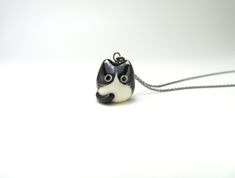 a small black and white cat necklace on a silver plated chain, with eyes closed