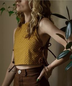 a woman standing next to a potted plant wearing a yellow top and brown pants