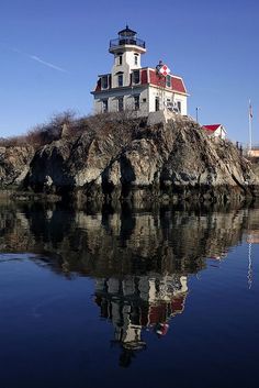 a light house sitting on top of a hill next to the ocean with a reflection in the water