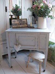 an old dresser with flowers and a sign on it next to a chair in front of a window