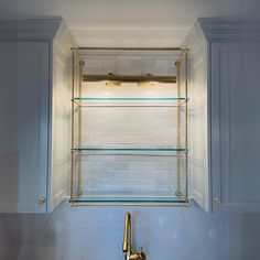 a bathroom sink with gold faucet and glass shelves above it