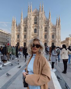 a woman standing in front of a large building with pigeons on the ground around her