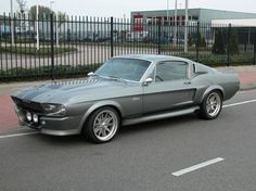 an old mustang muscle car is parked on the side of the road in front of a fence