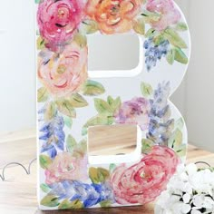 the letter b is decorated with flowers and has been placed next to a small white flower arrangement