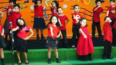 the children are singing on stage with microphones in front of them and an orange wall behind them