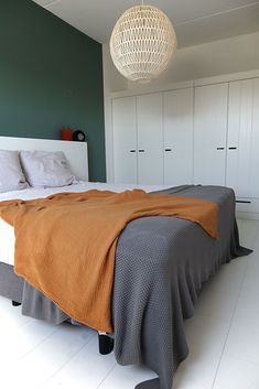 a bed with an orange blanket sitting on top of it next to white cupboards