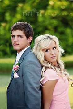 a young man and woman standing next to each other in front of some green trees