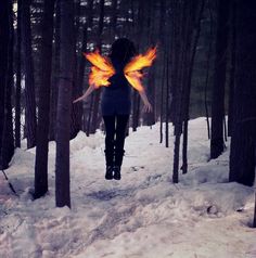 a woman is walking through the woods with fire wings