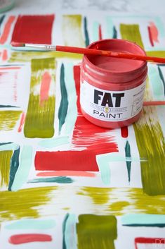 a red paint can sitting on top of a table next to a painting brush and paper