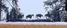 three horses are walking through the snow in front of some trees and pine trees on a snowy day