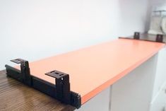 an orange shelf sitting on top of a wooden table next to a white wall and clock