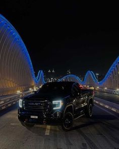 a black truck driving down a road next to a bridge at night with blue lights