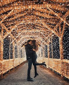 a man and woman kissing in an archway covered with christmas lights at the end of a walkway