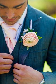 a man in a gray suit and pink flower boutonniere is adjusting his tie