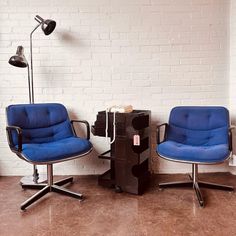 two blue chairs sitting next to each other in front of a white brick wall and floor