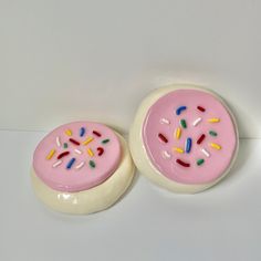 two pink donuts with sprinkles on them sitting next to each other