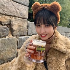 a woman wearing a bear hat and holding a mug in front of a stone wall