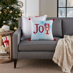 a christmas tree is in the background behind a gray couch with red and white pillows