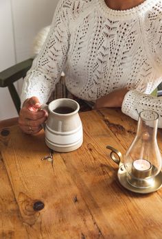 a woman sitting at a wooden table holding a coffee cup