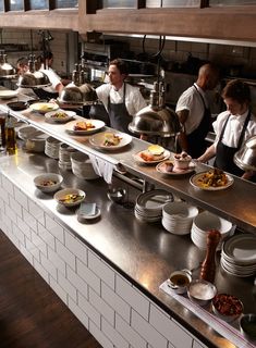 chefs preparing food in a restaurant kitchen with stainless steel counter tops and white brick walls