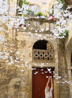 a man standing in front of a red door surrounded by white paper birds flying overhead