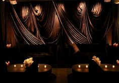 candles are lit in front of two couches with drapes on the wall behind them