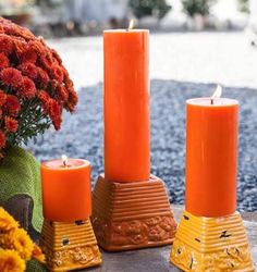 three orange candles sitting on top of a table next to some vases and flowers