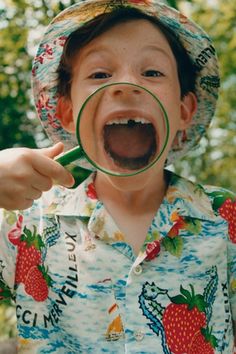 a young boy wearing a straw hat and holding a magnifying glass to his face