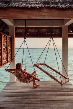 a little boy sitting in a hammock on a dock next to the ocean