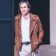 a man wearing a brown jacket and white shirt standing in front of a black door