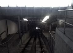 an empty subway tunnel with rails and railings leading into the light at the end