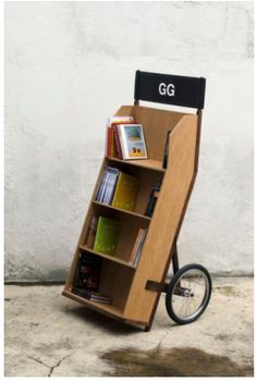 a wooden book cart with books on the front and wheels attached to it, against a white wall