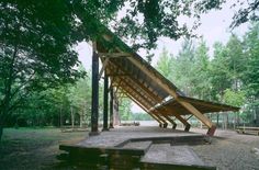 a wooden structure in the middle of a park with benches around it and trees surrounding it