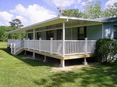 a house with white railings sitting in the grass next to some trees and bushes