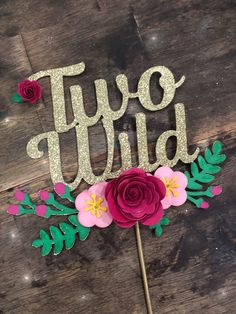 a cake topper that says two wild with flowers