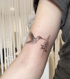 a small tattoo on the arm of a woman with a hummingbird flying over flowers