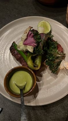 a white plate topped with meat and veggies next to a bowl of sauce