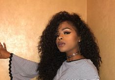 a woman with long curly hair wearing a striped shirt and choker posing in front of a wall